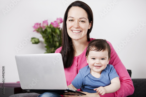 Photo: A mother using a laptop whilst holding her baby son on her lap A mother using a laptop whilst holding her baby son on her lap