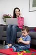 A woman using a laptop and phone at home, baby playing