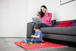 A mother using a laptop and phone, baby playing