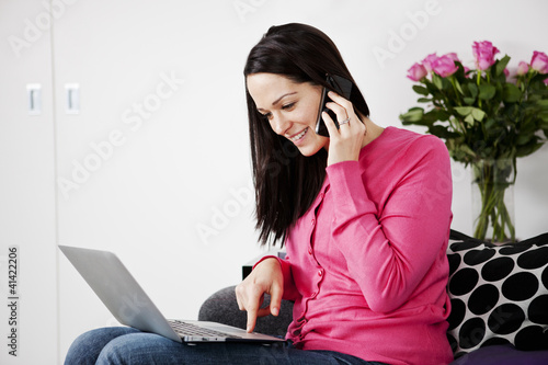 Photo: A woman using a laptop and mobile phone at home A woman using a laptop and mobile phone at home