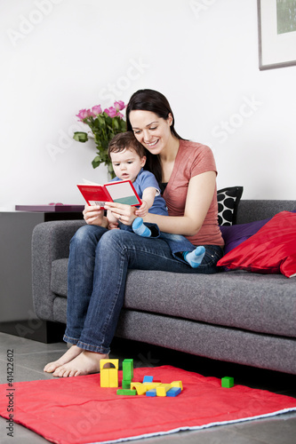 Photo: A mother and her baby son sitting on the sofa reading a book A mother and her baby son sitting on the sofa reading a book