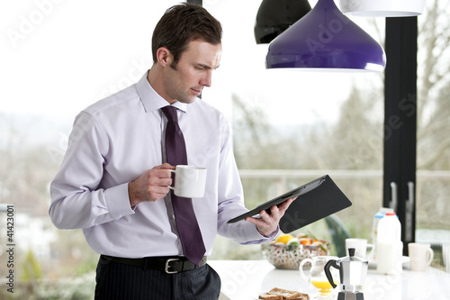Photo: A businessman standing in a kitchen holding a digital tablet A businessman standing in a kitchen holding a digital tablet