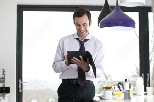 Photo: A businessman standing in a kitchen using a digital tablet A businessman standing in a kitchen using a digital tablet