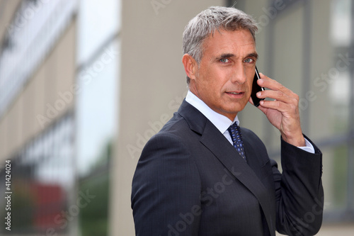 Photo: Mature businessman using a cellphone outside Mature businessman using a cellphone outside