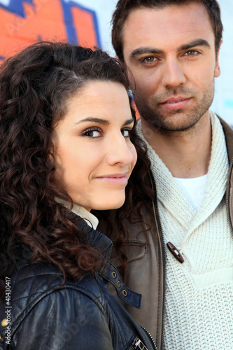 Photo: Couple posing by vandalized wall Couple posing by vandalized wall