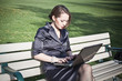 Businesswoman sitting on bench working on laptop in park