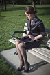 Business woman sitting on bench working on laptop in park