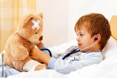 Foto: Krankes Kind untersucht Teddy mit Stethoskop Krankes Kind untersucht Teddy mit Stethoskop
