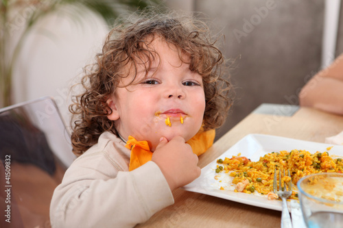 Photo: Little boy eating rice at kitchen table Little boy eating rice at kitchen table