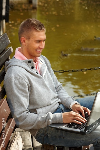 Photo: Happy man using laptop by lake Happy man using laptop by lake