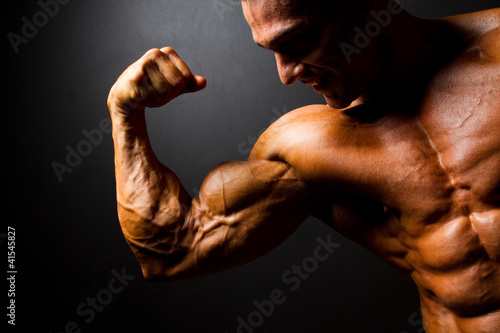 Photo: strong bodybuilder posing on black background strong bodybuilder posing on black background