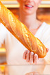 Bäckerin in ihrer Bäckerei verkauft Brot Baguette