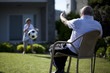 Grandfather sitting on chair and his grandson playing football