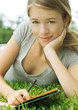 Young woman reclining in grass with notebook and pencil, portrait