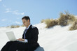Businessman sitting on sand dune, using laptop