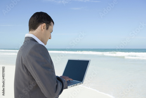 Foto: Businessman standing on beach, using laptop Businessman standing on beach, using laptop