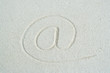 At" symbol traced in sand, close-up"