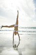 Young woman in bikini doing cartwheel on beach, full length