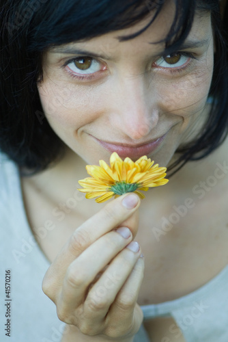Photo: Young woman smelling flower, smiling at camera, cropped, close-up Young woman smelling flower, smiling at camera, cropped, close-up