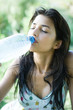 Young woman drinking from bottle of water, eyes closed, water dripping down face
