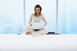 Woman sitting on windowsill using laptop, high rises in background