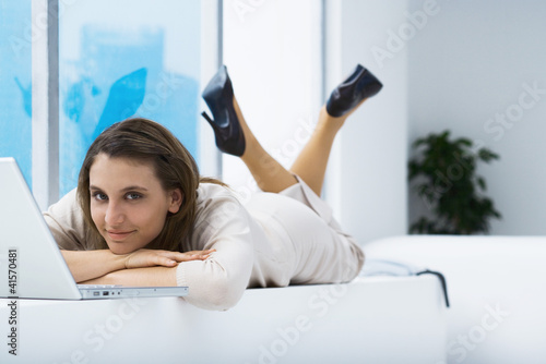 Photo: Woman lying on stomach near laptop, smiling at camera Woman lying on stomach near laptop, smiling at camera