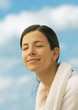 Woman wearing bathrobe, smiling with eyes closed, sky in background