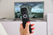 Foto: Frauenhand mit Fernbedienung und Fernseher Frauenhand mit Fernbedienung und Fernseher