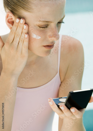 Foto: Woman applying sunscreen, looking into compact mirror Woman applying sunscreen, looking into compact mirror