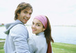 Young couple standing by lake, smiling over shoulder at camera
