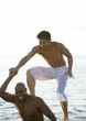 In sea, man stepping onto second man's shoulders
