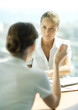 Photo: Two young female professionals sitting across from each other, having conversation, focus on woman listening in background Two young female professionals sitting across from each other, having conversation, focus on woman listening in background
