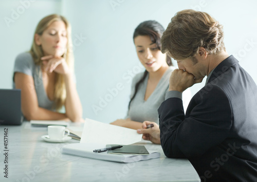 Photo: Mature man sitting at table with teenage girl and young female professional, reading document Mature man sitting at table with teenage girl and young female professional, reading document