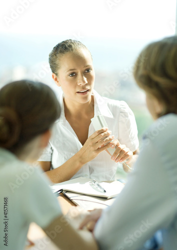 Photo: Young couple sitting across table from young female professional holding phone Young couple sitting across table from young female professional holding phone