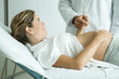 Pregnant woman lying on back, hand on stomach, holding doctor's hand, waist up