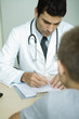 Doctor sitting across from boy, writing on clipboard