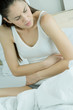 Young woman sitting on bed, arms across abdomen