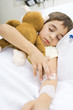 Boy lying in hospital bed, holding stuffed animal