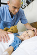 Girl lying in hospital bed, male nurse's hand on girl's forehead