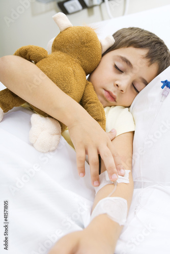 Photo: Boy lying in hospital bed, holding stuffed animal Boy lying in hospital bed, holding stuffed animal