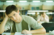 Male student studying in library, looking at camera