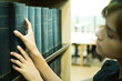 Female student taking reference book from shelf in library