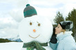 Teenage girl leaning against snowman, whispering, side view
