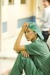 Medical worker sitting on floor in hospital corridor, holding head, looking away