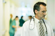 Male doctor looking away, head and shoulders, hospital corridor in background