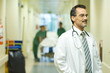Male doctor looking away, smiling, hospital corridor in background
