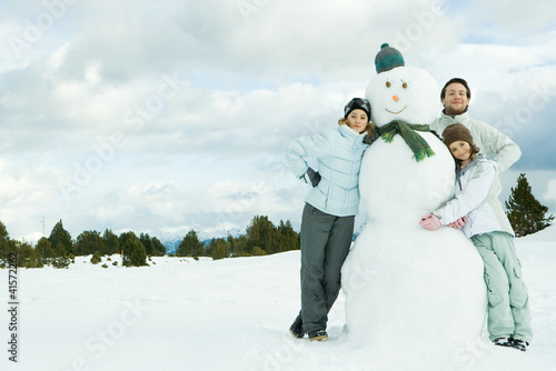 Foto: Three young friends leaning against snowman, smiling at camera, portrait Three young friends leaning against snowman, smiling at camera, portrait