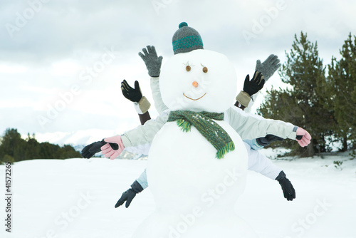 Photo: Young friends hiding behind snowman, arms out Young friends hiding behind snowman, arms out