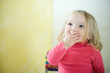 Blonde toddler girl covering mouth, looking up