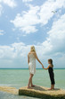 Mother and daughter standing on breakwater, holding hands, facing ocean